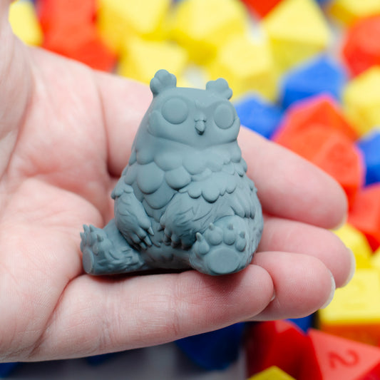 Resin print of a cartoony owlbear held in a hand, with colorful dice in the background.