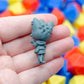 Gray miniature 3d printed figurine of the back of the catgirl, held in a hand with colorful dice in the background