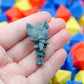 Gray 3d printed TTRPG miniature figurine of a catgirl with a school uniform and a fish bones in her mouth. It is held in a hand with colorful geometric blocks in the background
