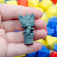 Small gray 3d printed miniature figurine of a cat girl holding a fish in a trashcan. It is held in a hand with colorful dice in the background.