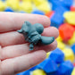 Gray 3d printed miniature figurine of a fox thief, held in a hand with colorful blurred background of dice