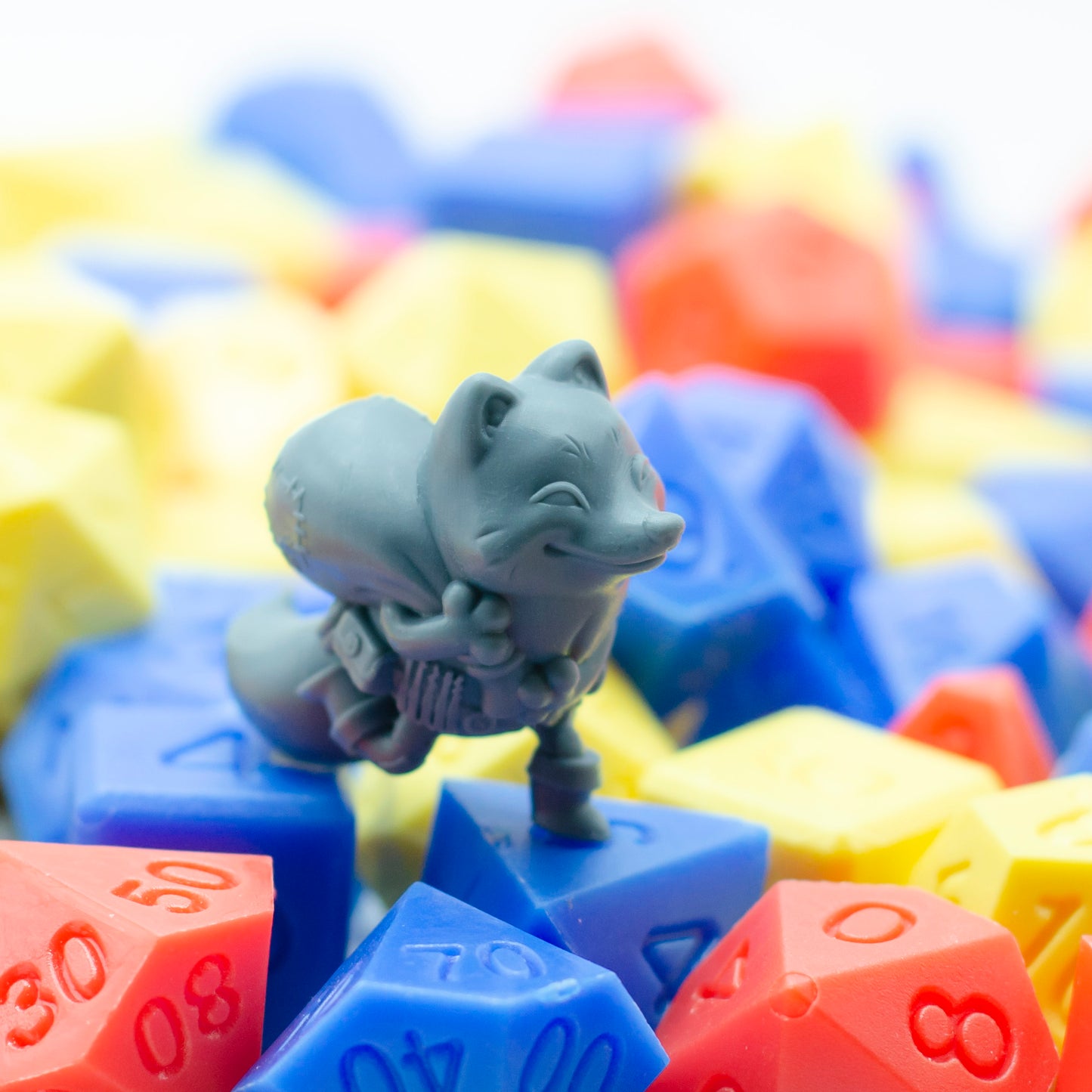 Gray 3d printed miniature figurine of a fox among colorful plastic dice