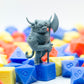 Gray 3d printed miniature figurine of a highland cattle minotaur with an axe, on top of colorful polyhedral dice.