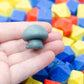 Gray 3d printed mushroom-shaped creature shown from the back, revealing its booty. It is held in a hand with colorful dice in the background.
