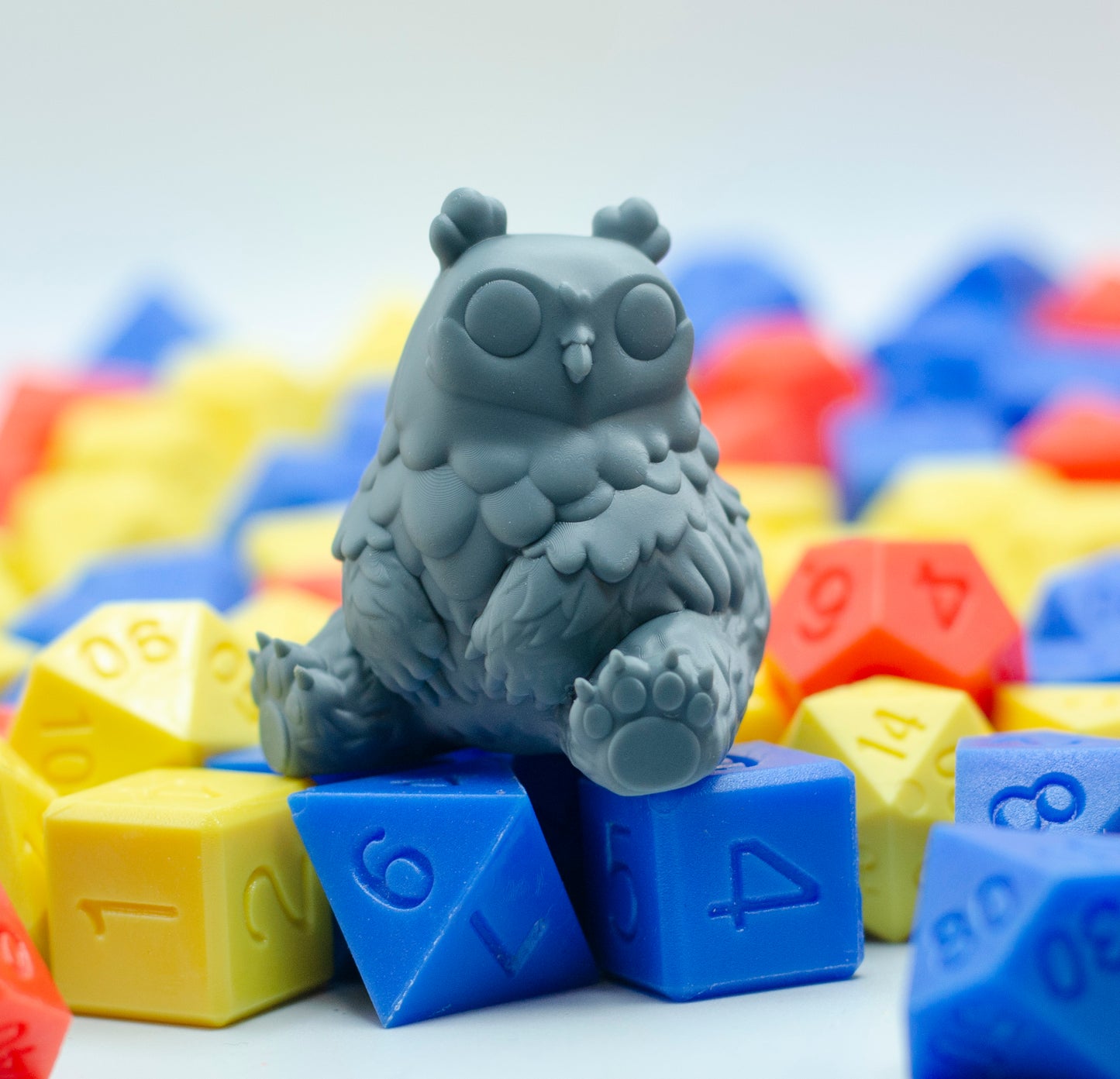 Resin print of a cartoony owlbear sitting on colorful dice.