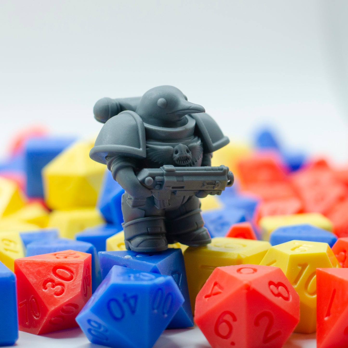 Gray 3d printed resin miniature of a space marine penguin in the style of Warhammer, surrounded by colorful polyhedral dice on a white background